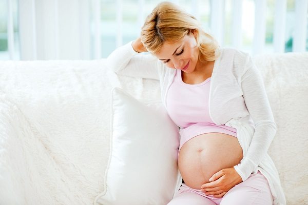 Pregnant blonde woman with hands over tummy.